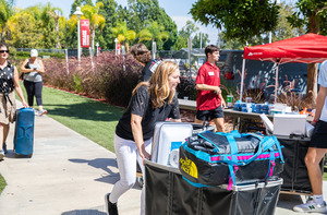 Students push carts of items across campus on a sunny day, ready to move in.