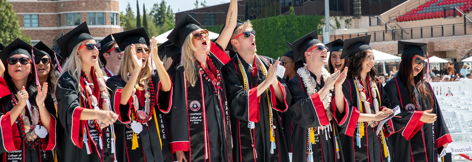 Graduating students in commencement regalia of black gowns, black caps, and red and black stoles.