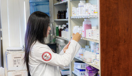 A student works in a pharmacy, examining a shelf of medicines.
