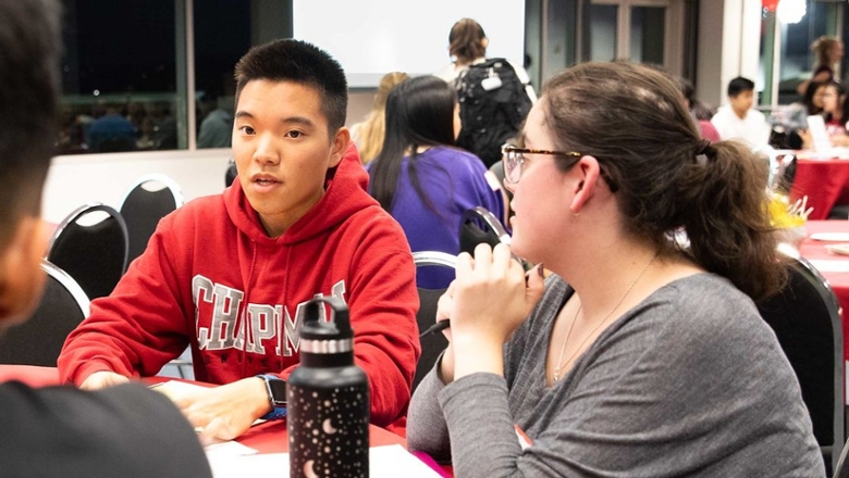 Students have a discussion in a classroom. There are laptops on the desk.