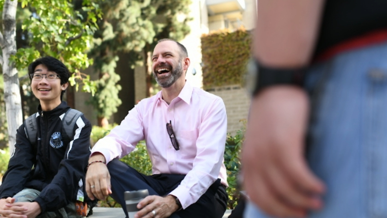 Faculty member laughs with students while sitting outside