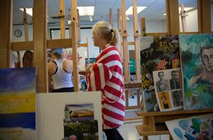 Students work in an art room, surrounded by easels containing paintings.