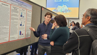 A student presents a research poster at a conference.