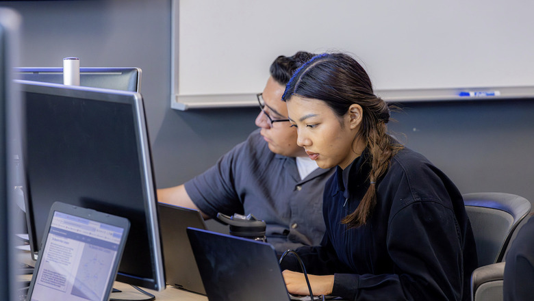 Two Finance students work on computers in a classroom.