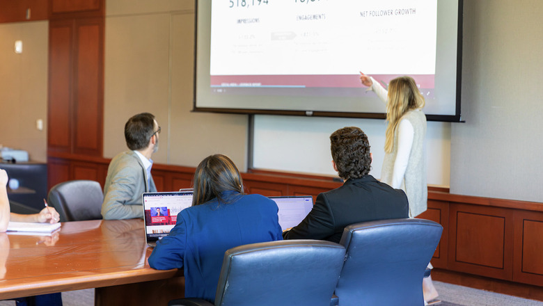 Students and a professor in a conference room going through a presentation.