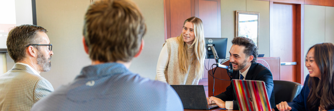 Students workign on a presentation with their professor in a conference room
