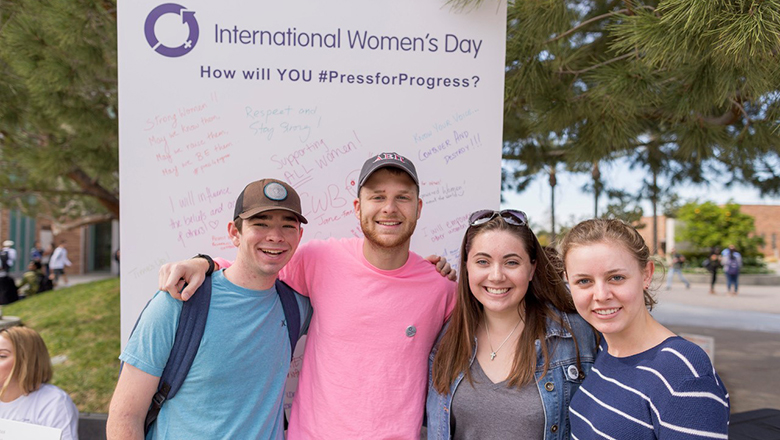 Four students in front of International Women's Day poster
