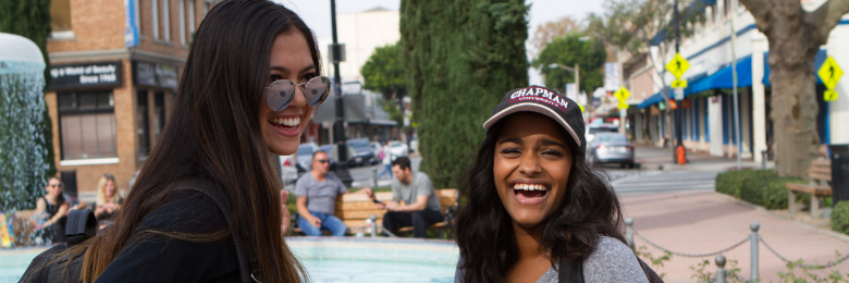 Two students stand in front of the fountain in the Orange Plaza