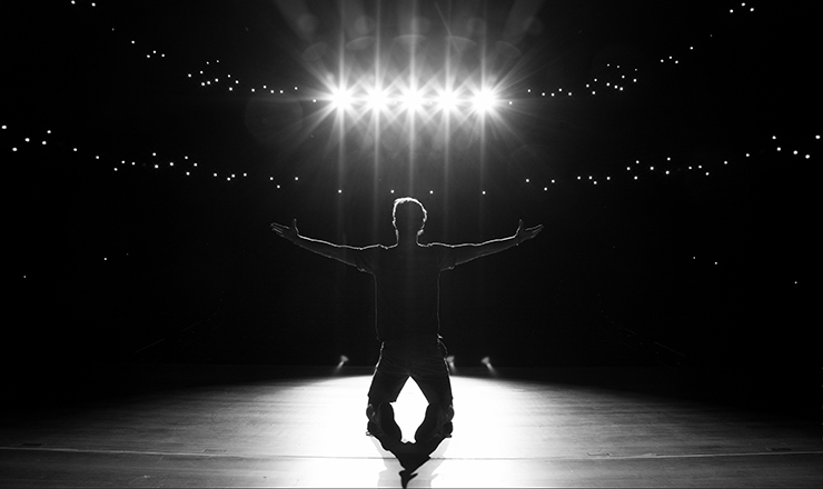 silhouette of man kneeling on a lighted stage.