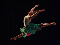 Dancer leaping up into the air against a black backdrop
