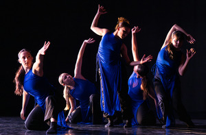 A number of students dance on a dimly lit stage.