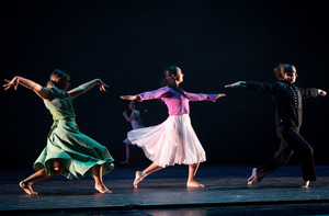 A number of students dance on a dimly lit stage.