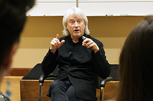 white-haired man in black lecturing to class