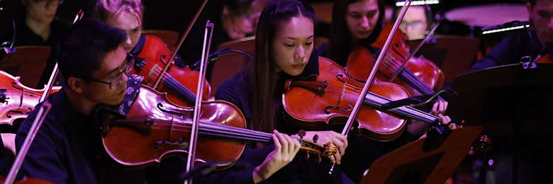 Closeup of two student violinists performing in low lighting.