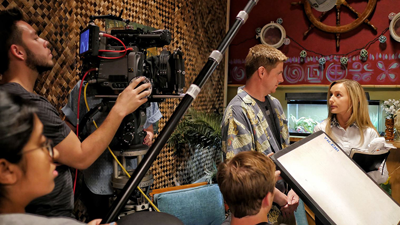 Two Chapman University students acting on set with a cameraman and other set staff in front of them