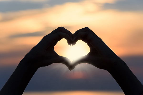 Two hands forming a heart shape in front of a sunset