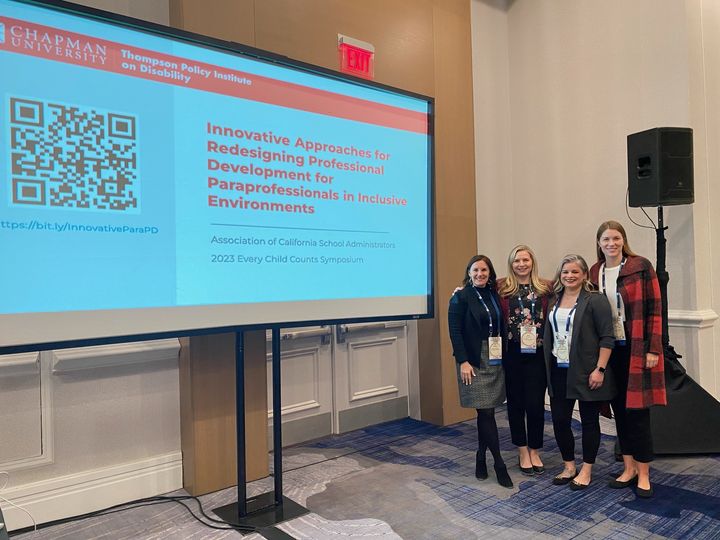 Jill Perez, Kari Adams, Audri Sandoval Gomez, and Shayne Brophy are standing next to each other in front of a screen with the title slide from their "Innovative Approaches for Redesigning Professional Development for Paraprofessionals in Inclusive Environments" presentation.