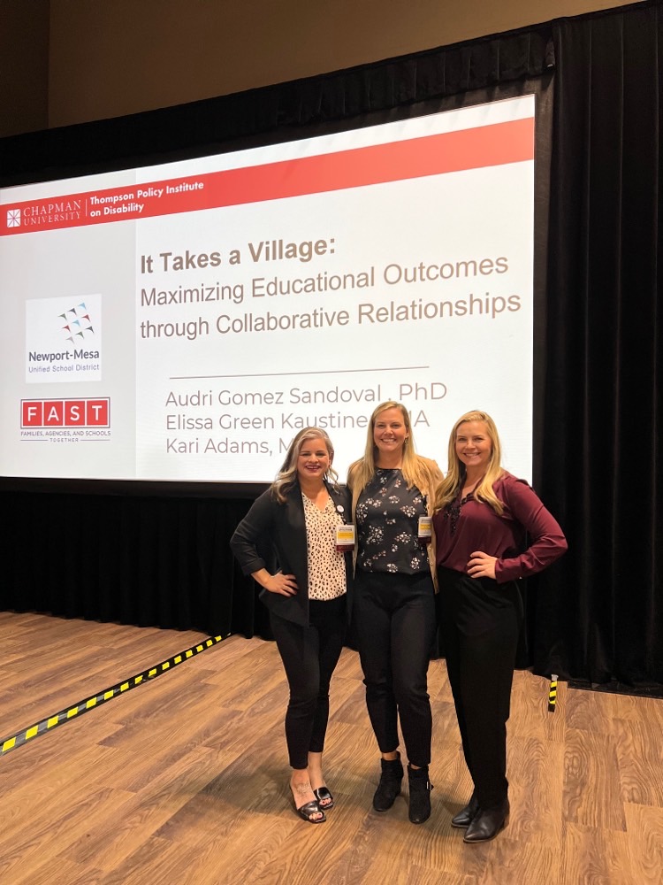 Audri Sandoval Gomez, Elissa Green Kaustinen, and Kari Adams are standing on stage with the presentation screen behind them. On the screen is the title of the presentation, "It Takes a Village: Maximizing Educational Outcomes Through Collaborative Relationships."