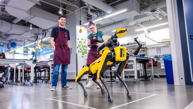 Two students next to a yellow robotic dog.