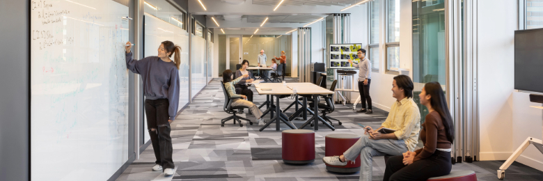 Student writes on whiteboard to present to other students in research lab