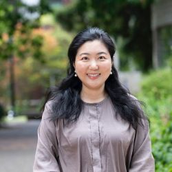 A woman with black shoulder lenght hair and black shirt with pearl earrings