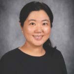 A woman with black shoulder lenght hair and black shirt with pearl earrings