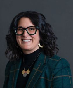Woman with black hair and sunglasses wearing a green blazer with a neclace.