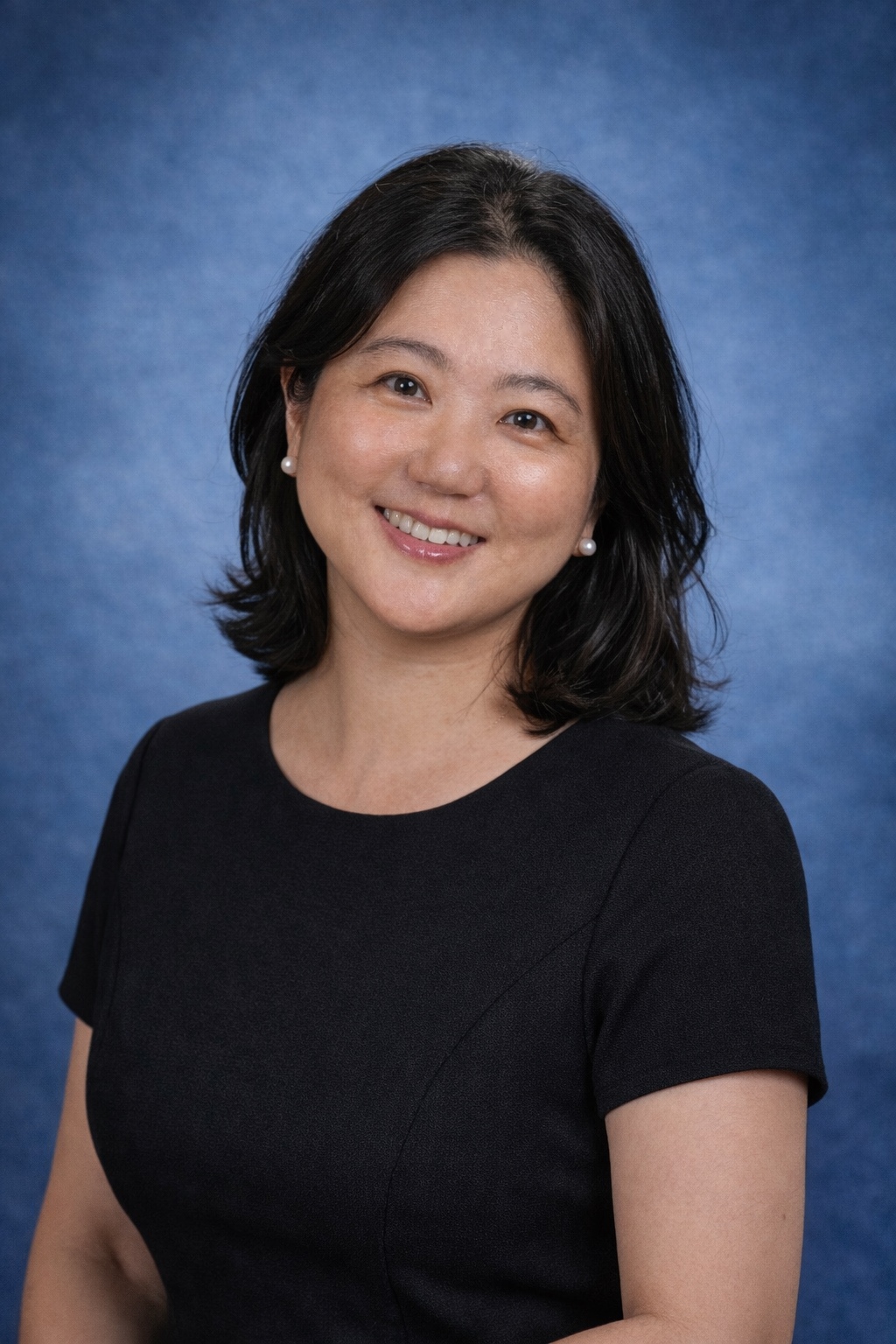 A woman with black shoulder lenght hair and black shirt with pearl earrings