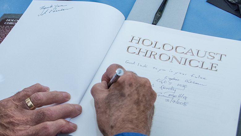Holocaust survivors writing inscription on title page of The Holocaust Chronicle