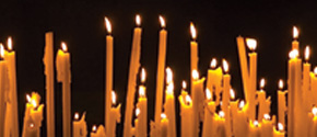 multiple thin, taper candles lit against a black background