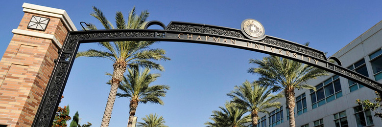 Schmid Gate at Chapman University on a clear day with palm trees and side of Beckman Hall in the background