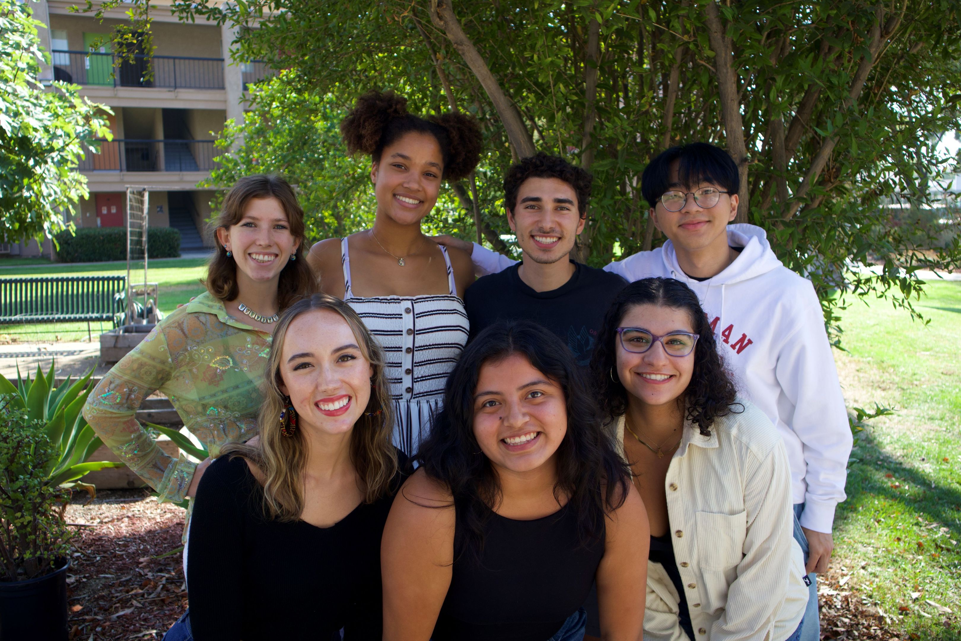 Seven students smiling together outside in front of nature.