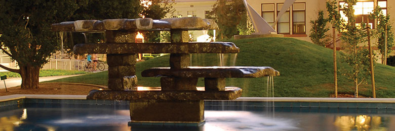 a rock fountain in a pool of water at Chapman University with grass in the background