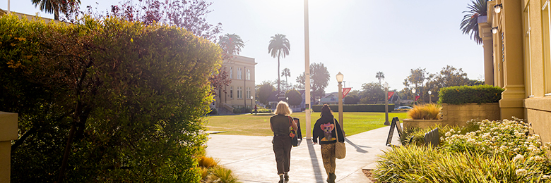 two women silhouetted walking on campus with the sun in front of them
