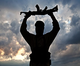 Silhouette of a man with a automatic rifle above his head outdoors at dusk